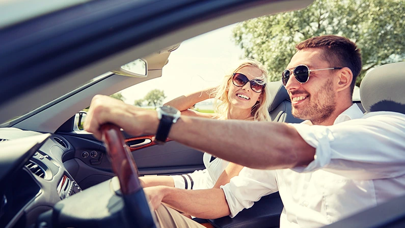 A couple smiles as they cruise in a convertible, the perfect way to rent a luxury car for a day.