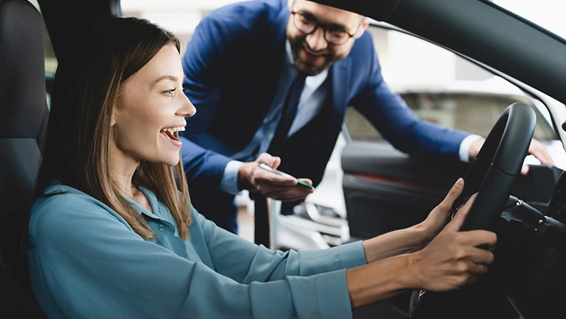 Satisfied happy caucasian female client customer woman sitting at the wheel of new car doing test-drive before renting a luxury car for a day